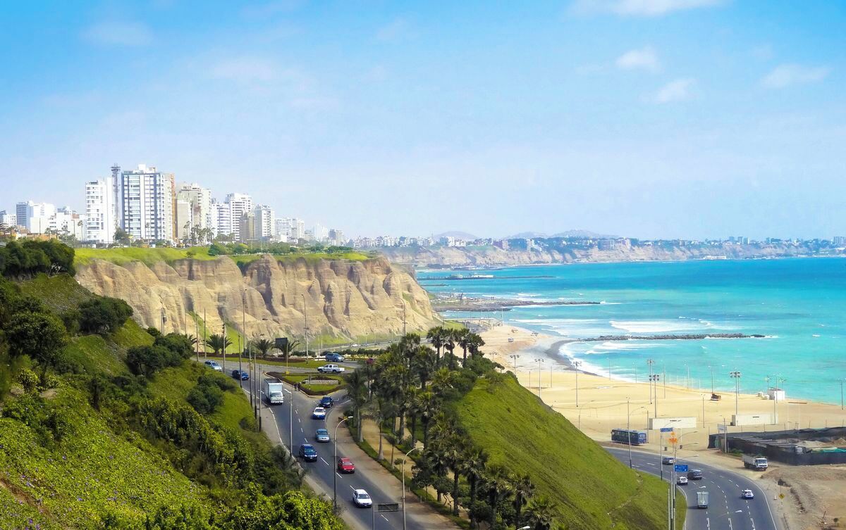 A coastal road with vehicles, a beach, and high-rise buildings in the background.
