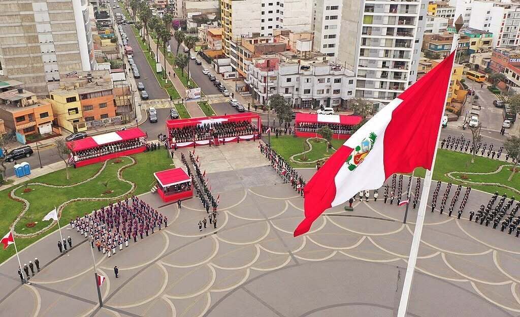 Ceremonia de izamiento de bandera con personal uniformado y una multitud en un entorno urbano.