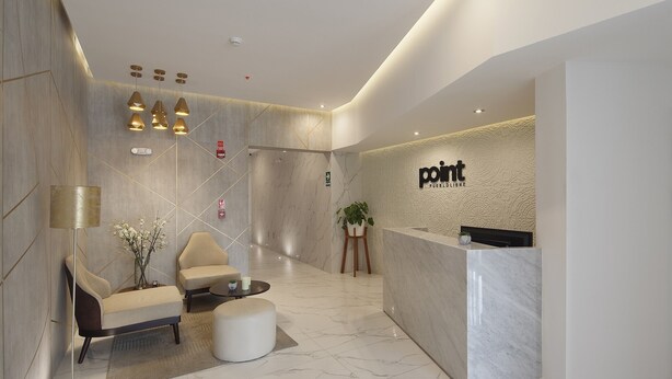 A modern reception area with a marble reception desk, a seating area with a sofa and armchairs, and pendant lighting. - Central Suite (Lima)
