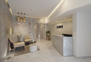 Uma área de recepção moderna, com um balcão de mármore, um espaço de espera com sofá e poltronas, e iluminação pendente.