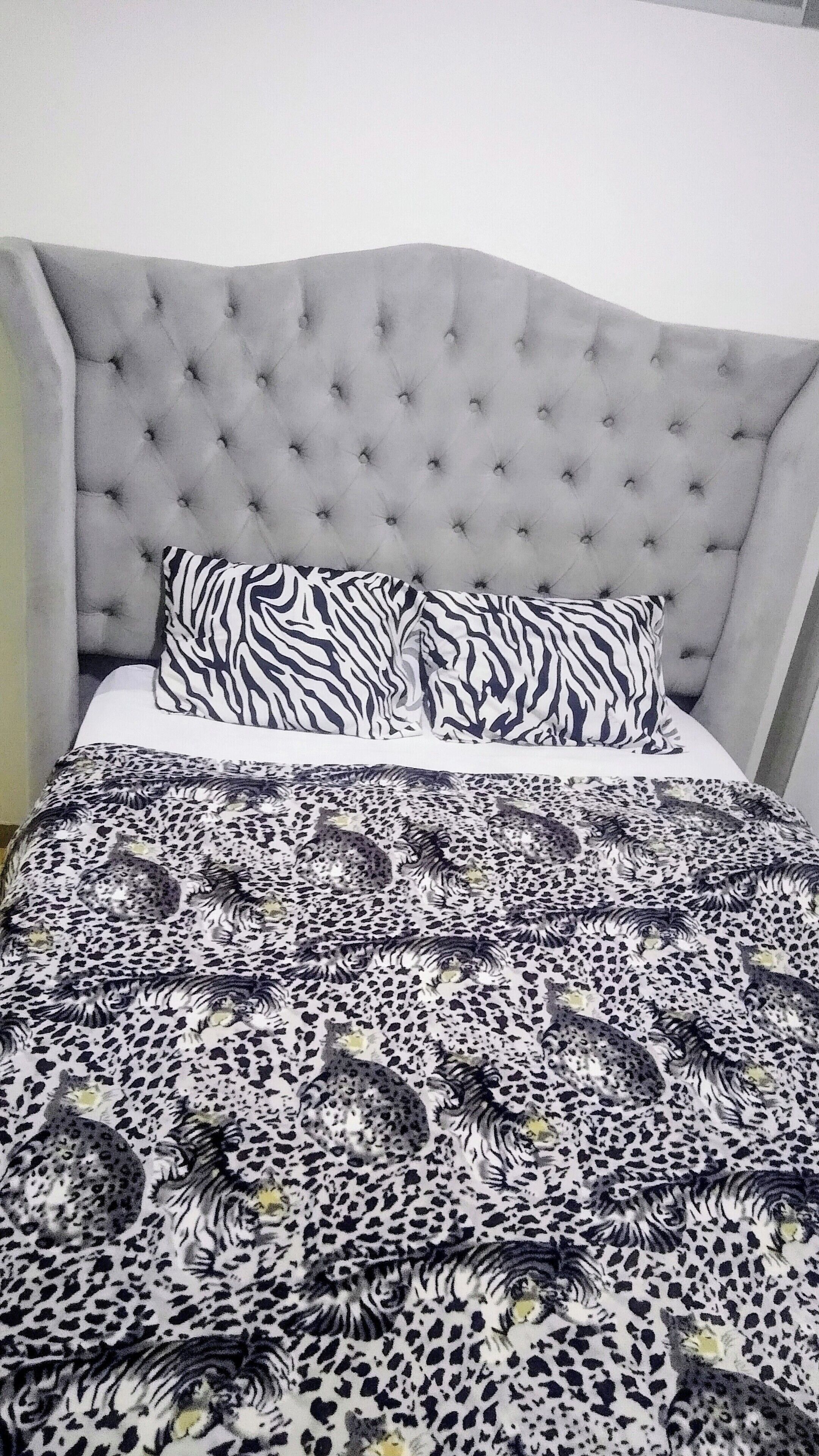 Una cama con cabecera capitonada, almohadas con estampado de cebra y colcha de leopardo.