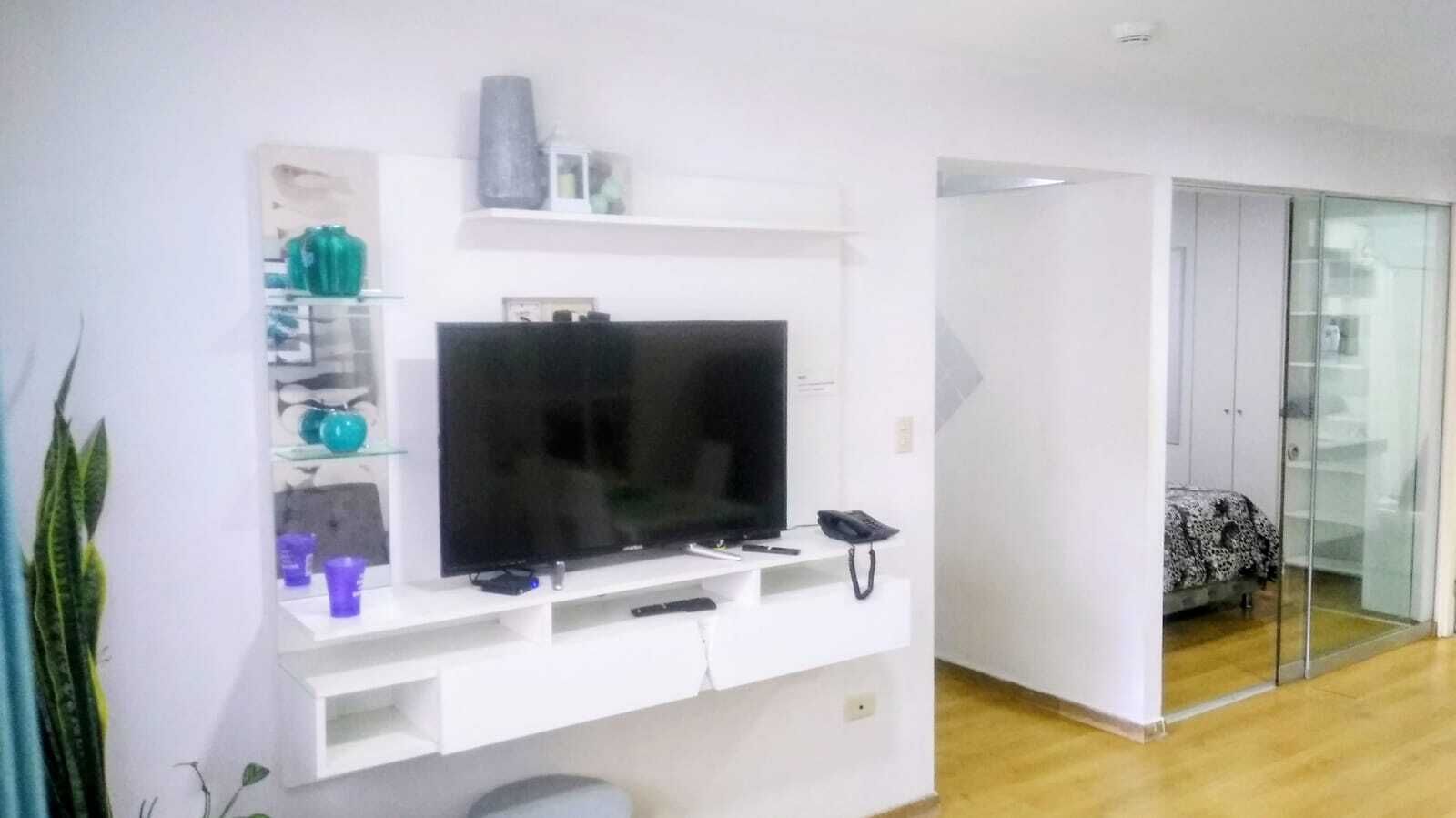 Un salon doté d’un téléviseur à écran plat, d’un meuble de rangement blanc, d’une armoire à porte vitrée et d’une plante.