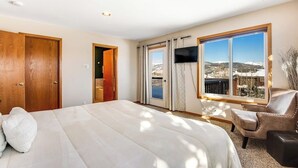 Ein Schlafzimmer mit Bett, Fernseher, Stuhl und einem großen Fenster mit Blick.