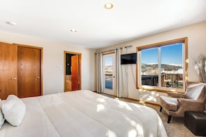 Ein Schlafzimmer mit Bett, Fernseher, Stuhl und einem großen Fenster mit Blick.