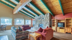 Un salon chaleureux avec une cheminée en pierre, des poutres apparentes et un téléviseur intégré dans un meuble en bois.