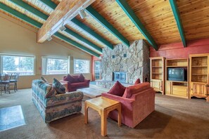 A cozy living room with a stone fireplace, wooden beams, and a television in a wooden cabinet. - Mountaintop condo with private balcony (Silverthorne)