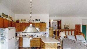 Une cuisine avec des meubles en bois, un réfrigérateur blanc, une lampe suspendue et un coin repas comprenant un canapé et une table.