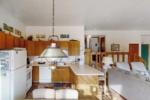 A kitchen with wooden cabinets, a white refrigerator, a hanging lamp, and a dining area with a sofa and table. - Mountaintop condo with private balcony (Silverthorne)