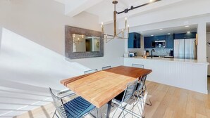 Une cuisine moderne avec des meubles de couleur sombre, un îlot central et un coin repas comprenant une table en bois et des chaises en métal.