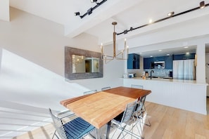 Eine moderne Küche mit dunklen Schränken, einer zentralen Kochinsel und einem Essbereich mit Holztisch und Metallstühlen.