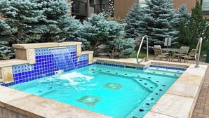 Une piscine rectangulaire bordée de mosaïques bleues, agrémentée d’une petite cascade et dotée d’un espace détente avec des chaises et une table.