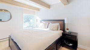 Une chambre à coucher avec un lit, une table de chevet, une lampe et une fenêtre donnant sur un beau paysage.