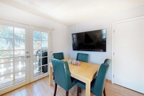 Ein Essbereich mit einem Holztisch und vier Stühlen, einem flachbildfernseher an der Wand und einer Schiebeglastür, die auf einen Balkon führt.