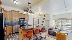 A modern kitchen with a central island, bar stools, and a dining area with a sofa and coffee table. - Kutuk 108 Ski, stay, & play - Steamboat Springs getaway only steps away from the mountain (Steamboat Springs)