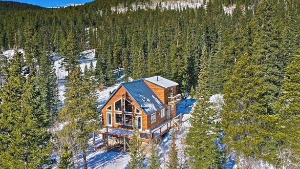 Una cabaña con una terraza grande, rodeada de un bosque denso y nieve.