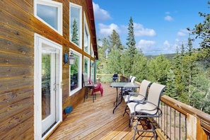 A wooden deck with a table and chairs, a glass door, and a view of trees and hills. - Secluded Mountain Cabin w/ Hot Tub, Fireplace & Stargazing Deck near Breck (Alma)