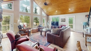 Amplia sala de estar con un televisor grande, asientos cómodos y ventanas amplias que ofrecen vistas al exterior.