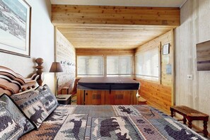Ein gemütliches Zimmer mit Holzbalkendecke, einem Bett mit gemusterten Kissen, einer Bank und einem kleinen Tisch mit einer Lampe.