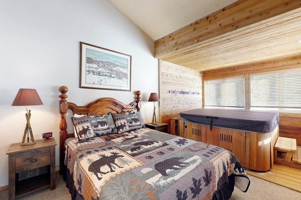 A bedroom with a wooden headboard, a large bed with a quilt, a wooden cabinet, a hot tub, and a framed picture on the wall.