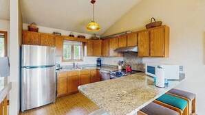 Eine Küche mit Holzausstattung, einem Edelstahlkühlschrank, einer Granit Arbeitsplatte und einer Pendelleuchte.