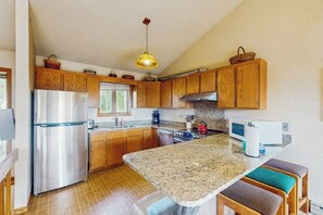 Eine Küche mit Holzausstattung, einem Edelstahlkühlschrank, einer Granit Arbeitsplatte und einer Pendelleuchte.