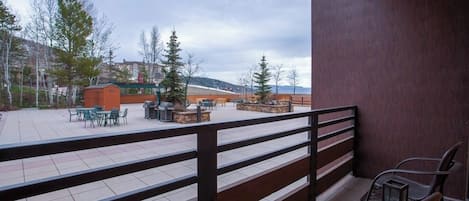 Ein möblierter Außenbereich mit Holzgeländer und Blick auf ein Gebäude sowie Bäume im Hintergrund.
