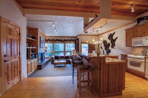 Eine rustikale Küche mit Holzschränken, einer zentralen Kochinsel, einem Kamin und einem Essbereich mit einer Couch und Stühlen.