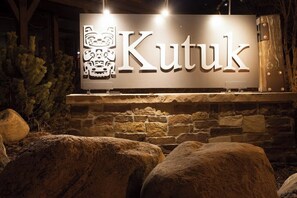 Ein Schild mit der beleuchteten Aufschrift 'Kutuk', vor einer Steinwand mit großen Felsen im Vordergrund.