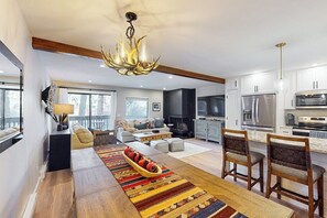 Ein modernes Wohnzimmer mit Kamin, ein Essbereich mit einem gemusterten Teppich und eine Küche mit Edelstahlgeräten.