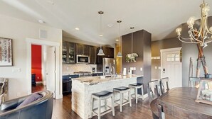 Een moderne keuken met een centraal eiland, barkrukken en een eettafel met stoelen.