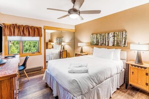 Ein Hotelzimmer mit Bett, Schreibtisch, Stuhl, Deckenventilator und Bildern an der Wand.