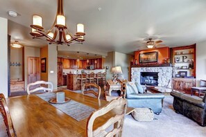 A spacious living area with a dining table, sofas, a fireplace, and a kitchen in the background. - Luxury Ski-In/Out Condo w/Free WiFi, Fireplace, W/D, Shared Pool, Hot Tub, Grill (Steamboat Springs)