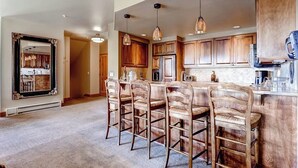 Una cocina con armarios de madera, una isla central con taburetes de bar, iluminación colgante y un espejo grande en la pared.