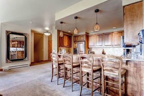 A kitchen with wooden cabinets, a central island with bar stools, pendant lighting, and a large mirror on the wall. - Luxury Ski-In/Out Condo w/Free WiFi, Fireplace, W/D, Shared Pool, Hot Tub, Grill (Steamboat Springs)