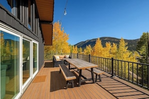 A deck with a table and benches, overlooking a mountainous landscape with autumn foliage.