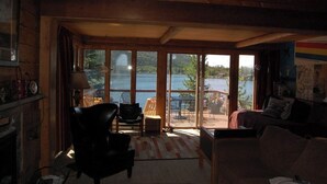 A cozy room with a large sliding glass door leading to an outdoor patio with a table and chairs. - Original charmer with expansive waterfront deck, dock, fireplace - walkable area (Grand Lake)