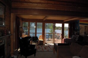 A cozy room with a large sliding glass door leading to an outdoor patio with a table and chairs. - Original charmer with expansive waterfront deck, dock, fireplace - walkable area (Grand Lake)