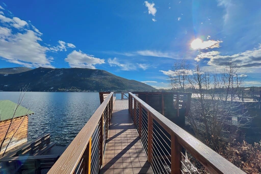 A wooden pier extending over calm water with mountains in the background.