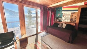 A cabin with a bed, a chair, a wooden ceiling, a window, and a poster on the wall. - Original charmer with expansive waterfront deck, dock, fireplace - walkable area (Grand Lake)