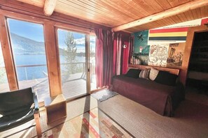 A cabin with a bed, a chair, a wooden ceiling, a window, and a poster on the wall. - Original charmer with expansive waterfront deck, dock, fireplace - walkable area (Grand Lake)