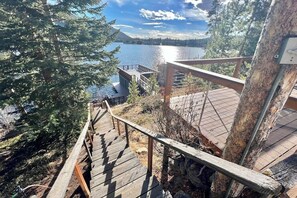 A wooden staircase leading to a viewing platform overlooking a lake, surrounded by trees. - Original charmer with expansive waterfront deck, dock, fireplace - walkable area (Grand Lake)