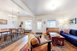 Ein Wohnzimmer mit einer Couch, einem Couchtisch, einem Esstisch, Stühlen und einer Deckenleuchte.