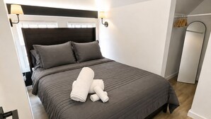 A modern bedroom with a dark grey bed, a headboard, a bedside lamp, and a large mirror.