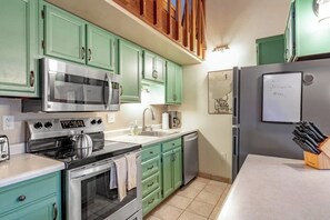 Eine Küche mit türkisgrünen Schränken, Edelstahlgeräten, einem Geschirrspüler und einem Kühlschrank mit einer Tafel.