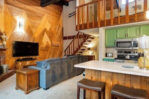 Eine moderne Küche mit grünen Schränken, einem großen Fernseher und einer Holzbalkendecke.