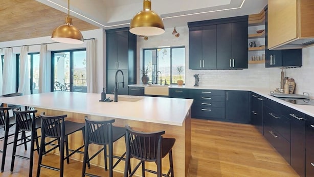 A modern kitchen with dark cabinetry, a large island with bar stools, and pendant lighting. - Modern home with a hot tub, game room and fabulous deck space! (Tabernash)