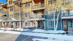 Un hotel de varios pisos con balcones, un estacionamiento y nieve en el suelo.