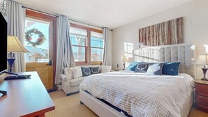 Un dormitorio con cama, escritorio, silla, ventana con cortinas y una obra de arte colgada en la pared.