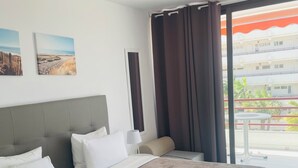Ein Hotelzimmer mit zwei Betten, einem Fenster mit Vorhängen, einem kleinen Tisch und einem Bild an der Wand.