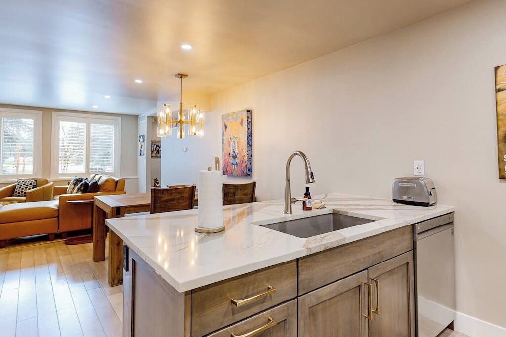 A modern kitchen with a large island, wooden cabinets, and a dining area with a sofa and table.